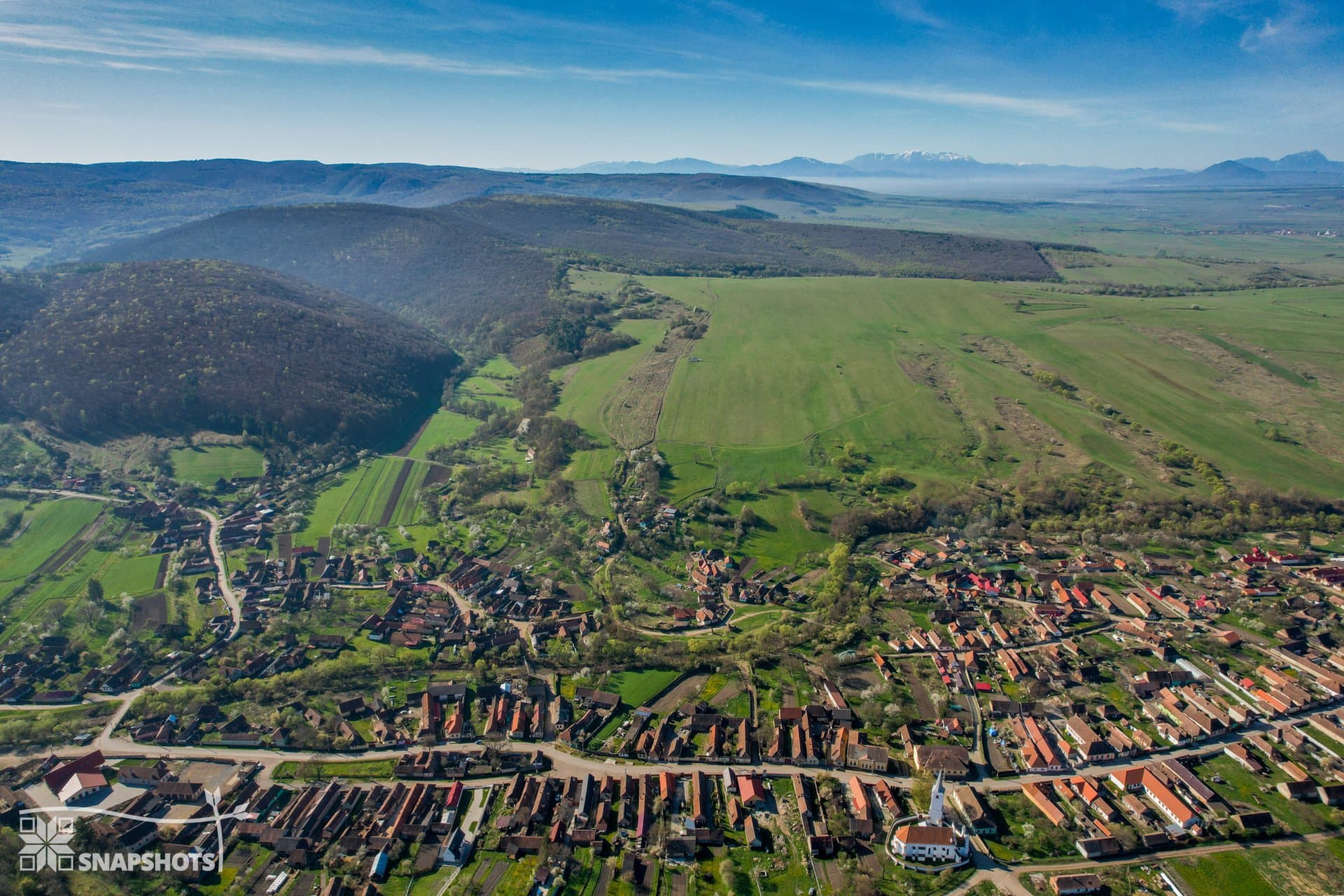 Aerial view of a Transylvanian village nestled at the foot of forested hills